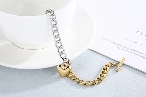 Detail of two-tone gold and silver heart pendant bracelet with OT toggle clasp on white background