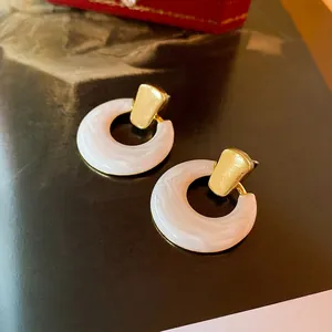 Modern gold hollow hoop earrings with white marble resin drop on dark background