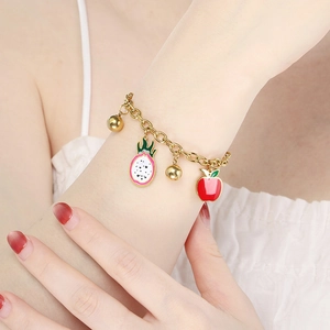 Close-up of 18K gold chain bracelet with dragon fruit and apple charms on model wrist