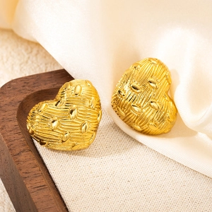Macro shot of gold heart-shaped stud earrings with woven texture and embossed details