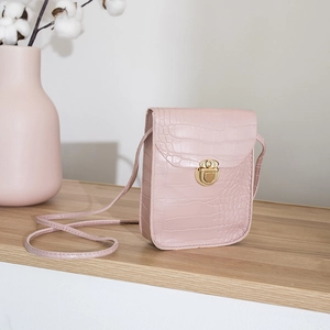 Pink crocodile pattern crossbody bag with gold rotating lock on wooden surface