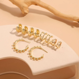 Detailed set of 14K gold plated heart earrings and zircon cuffs on beige display