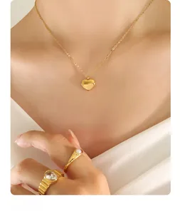 Close-up of a gold heart pendant necklace and pearl ring on a model with white fabric background