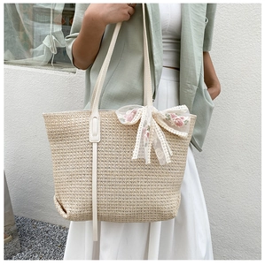 Detail of straw tote bag with lace bow accessory and long white faux leather shoulder strap