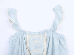 Close-up of light blue summer top featuring white floral embroidery and ruffle straps