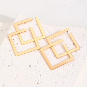 Close-up of golden geometric diamond stud earrings on a white marble stone surface