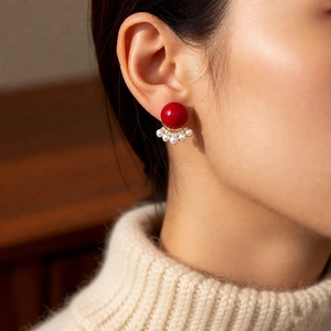 Close-up of model wearing 18k gold pearl earrings with a large red bead and zircons