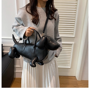 Detail of dachshund-shaped black leather handbag worn as a crossbody bag with gray hoodie
