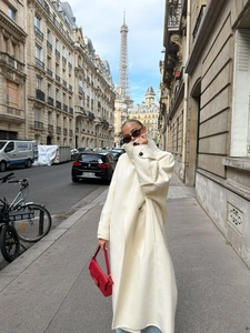 Detail of a white long wool coat paired with a red faux leather handbag in Paris