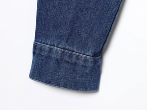 Detailed close-up of dark blue denim jacket cuff with precise double-needle stitching