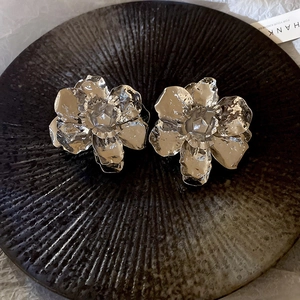 Detailed view of silver pleated metal flower earrings on a textured black base
