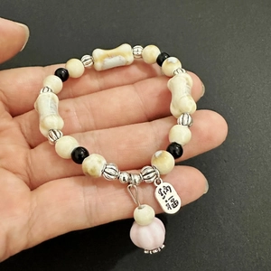 Detail eines Perlenarmbands in Knochenform mit Lotus-Anhänger und Glücksschild