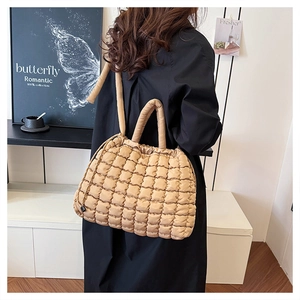 Detail of a beige quilted tote bag showing padded texture and shoulder strap on model