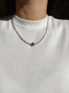 Close-up of a silver碎银子 neck chain with a dark grey pearl pendant on a model