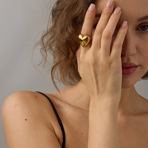 Detailed view of large gold heart ring with polished mirror finish on model's hand
