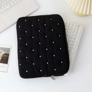 Flat lay of a black quilted polka dot laptop sleeve on a modern workspace desk