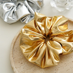 Close-up of metallic silver and gold scrunchies with pleated texture on stone tray