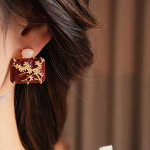 Detail of red enamel rectangular earring with golden floral emboss and pink gemstone