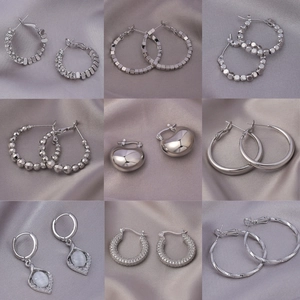 Nine pairs of elegant silver earrings including hoops and studs on grey silk background
