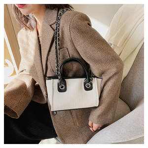 Chic beige canvas bucket bag with black leather trim and chain strap styled on a model