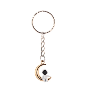 Detail of creative astronaut sitting on a gold moon pendant keychain with silver chain