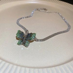 Close-up of butterfly pendant with green faceted crystals on a silver mesh chain necklace