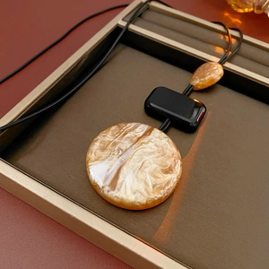 Macro detail of brown marble resin pendant on a black cord in a luxury jewelry tray