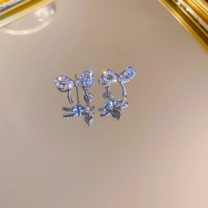 Détail de boucles d'oreilles nœud argentées avec zircons posées sur un socle miroir
