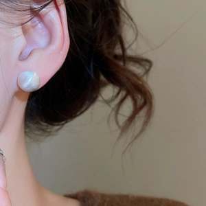 Close-up of minimalist brushed silver stud earring with cat-eye stone on model's ear