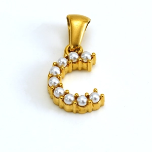Détail d'un pendentif lettre C doré orné de perles blanches sur une surface polie