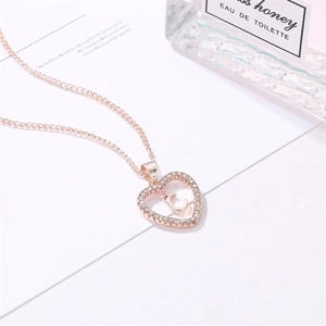 Collier cœur en or rose avec diamants étincelants et lettre C sur support blanc pur