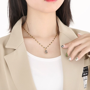 Detail of gold chain necklace with black beads and silver seashell pendant worn by a model