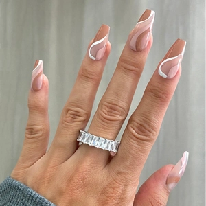 Close-up of long coffin press-on nails in nude pink with white wavy lines and a diamond ring