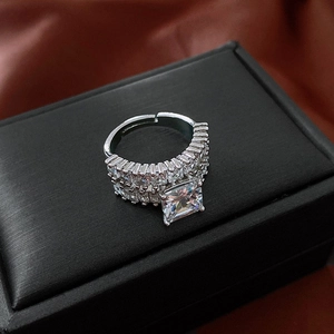 Macro shot of silver ring with square zircon and dual-row diamonds on black box