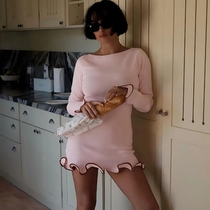 Detail of pink long sleeve mini dress featuring a brown ruffle hem in kitchen setting