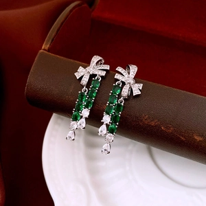 Macro view of bow-shaped tassel earrings with green gemstones and sparkling zircons