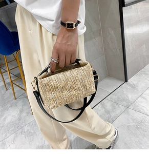 Detail of hand-held beige straw bag with black leather strap and textured weave pattern