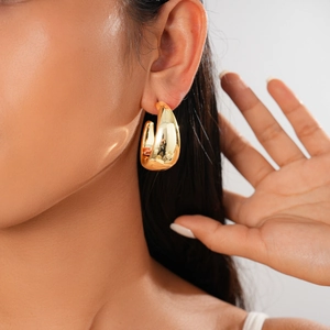 Detailed view of chunky golden teardrop earrings with a polished mirror finish on model