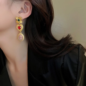 Detalle de pendientes vintage dorados con corazón rojo y camafeo de retrato en modelo
