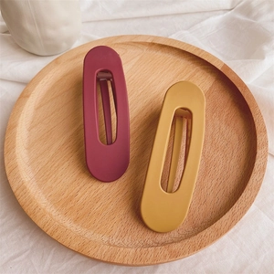 Detail of matte hollow hair clips in burgundy and mustard yellow on a wooden tray