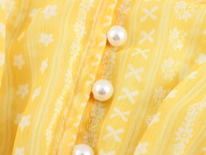 Detailed view of yellow floral fabric with delicate white pearl buttons on dress