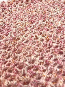 Macro detail of knit crochet fabric with pink and white hollow mesh and small sequins