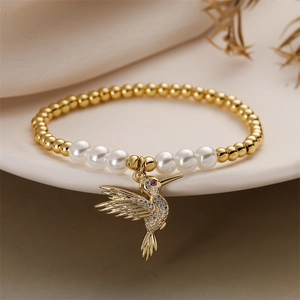 Gros plan d'un bracelet de perles dorées avec pendentif colibri sur un plat en céramique