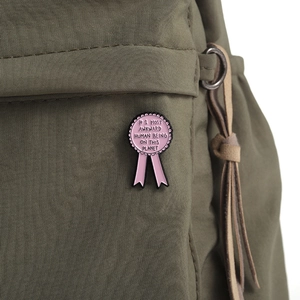 Détail macro d'une broche en émail rose en forme de ruban sur un sac à dos vert