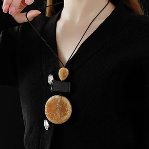 Detail of a brown resin teardrop geometric pendant on a long black adjustable cord
