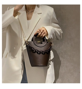 Detail of dark brown leather bucket bag with round handle and gold chain strap on white suit