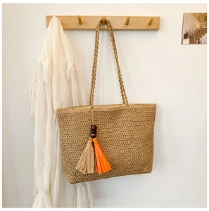 Close-up of woven straw tote bag featuring decorative orange and beige tassels
