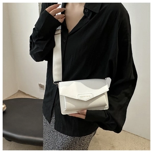 Close-up of white flap crossbody bag with wide strap on a model wearing black