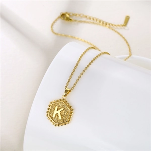 Macro detail of golden hexagonal letter K pendant with matte texture and fine chain