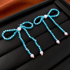 Detail of blue beaded bow earrings with white imitation pearls on black display tray